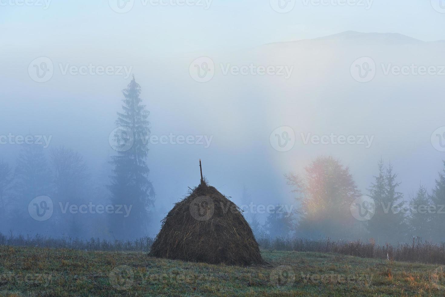 erstaunliche Berglandschaft mit Nebel und Heuhaufen im Herbst foto