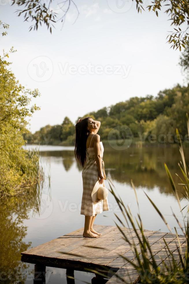 junge Frau, die auf dem Holzsteg am ruhigen See steht foto