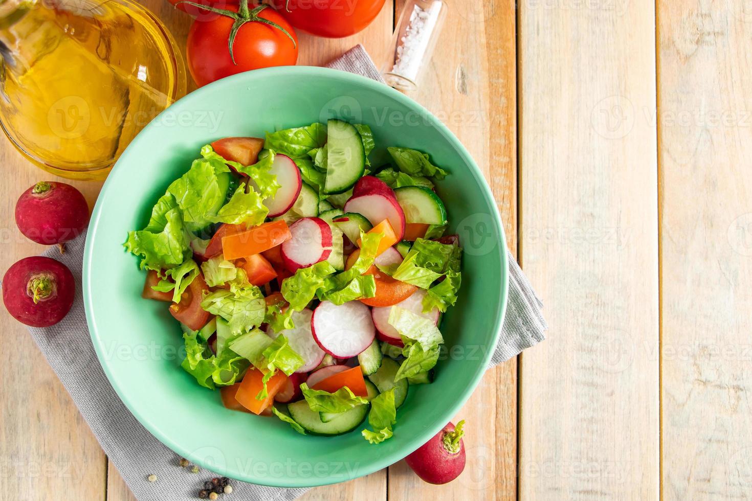 Salat aus frischem Gemüse mit Olivenöl in Keramikschale auf Holzhintergrund. foto