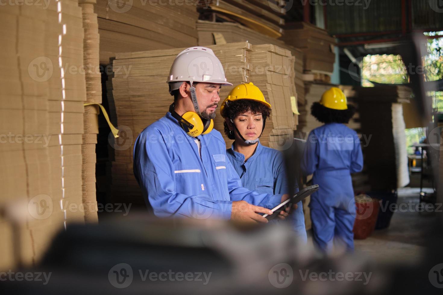 asiatischer ingenieur in sicherheitsuniform und schutzhelm und mitarbeiterin inspizieren lagerung, lagerbestellung im werkslager, stapel von stapelkartonherstellung, produktmanagement in der industrie. foto