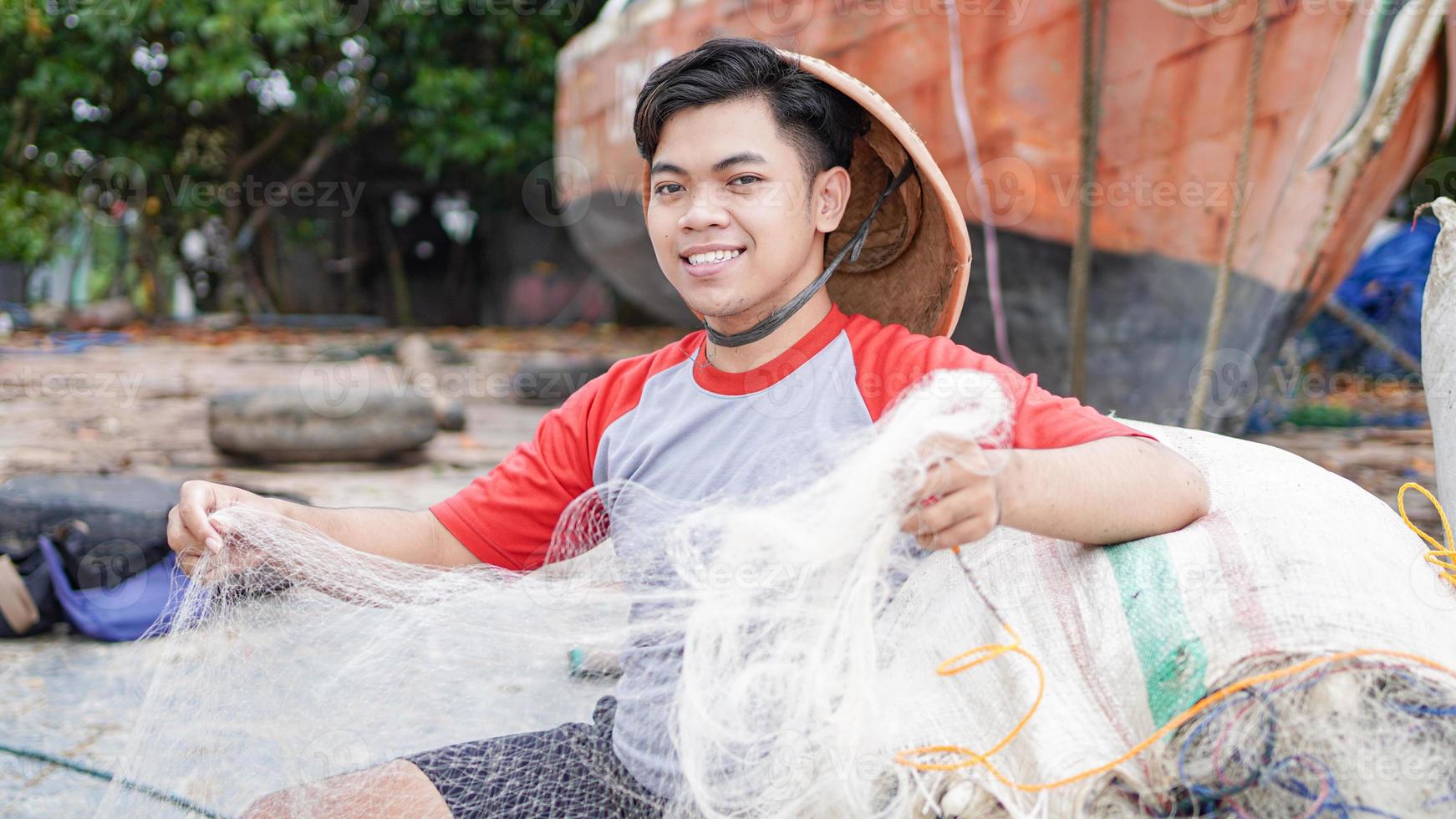 Porträt eines jungen männlichen Fischers, der ein Fischernetz am Strand vorbereitet foto