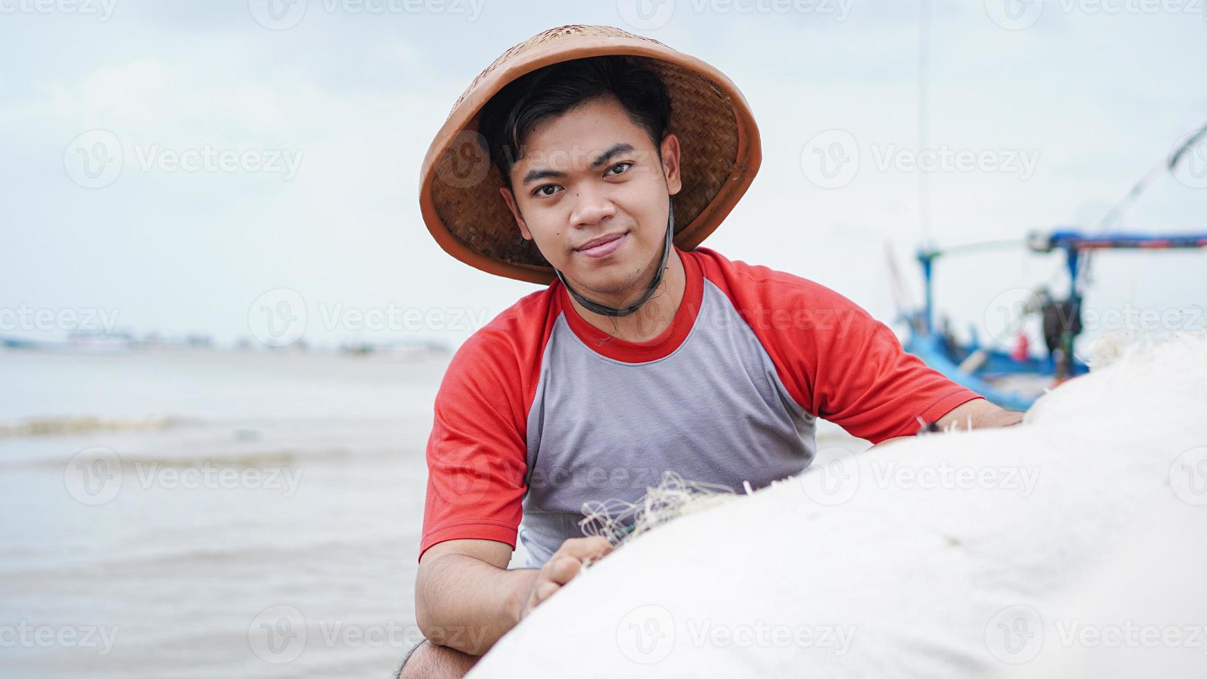 Porträt eines jungen männlichen Fischers, der ein Fischernetz am Strand vorbereitet foto