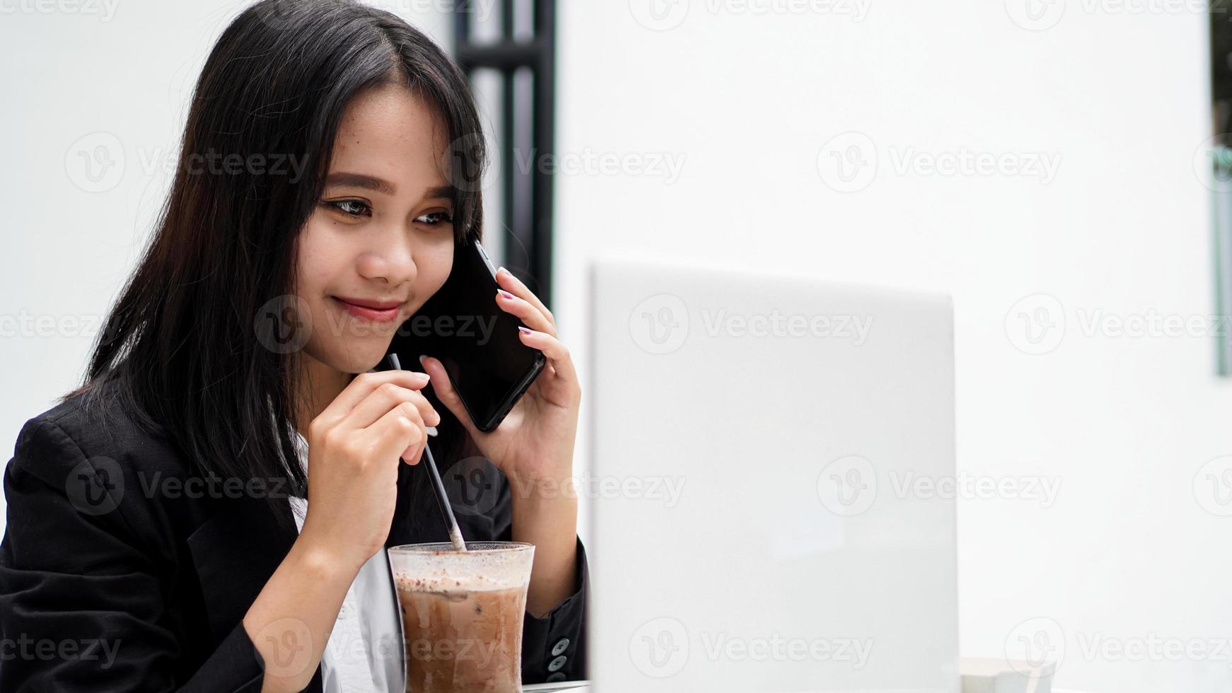 asiatische Geschäftsfrau, die Kaffee trinkt und im Café mit dem Smartphone spricht foto