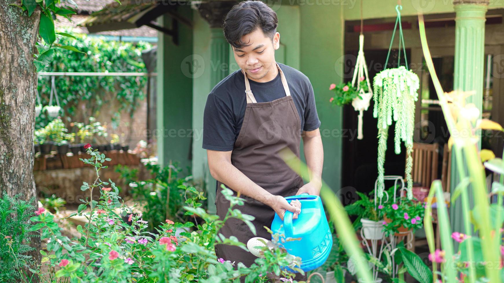 asiatischer mann, der sich darum kümmert, blumen im hausgarten zu gießen foto