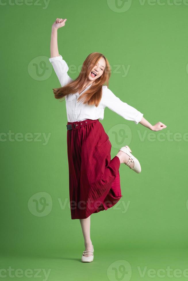 schöne junge asiatische frau, die auf grünem hintergrund tanzt und aufwirft foto