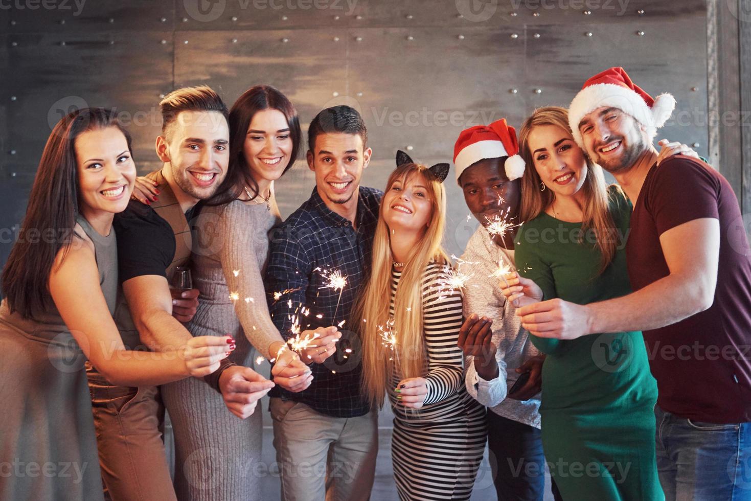 Party mit Freunden. Gruppe fröhlicher junger Leute, die Wunderkerzen und Champagnerflöten tragen foto