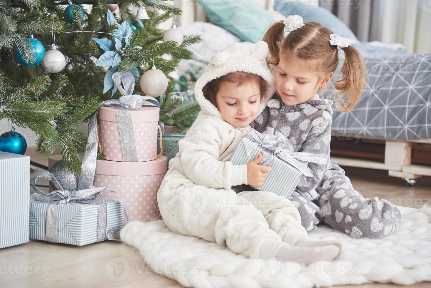 zwei kleine schwestermädchen öffnen morgens ihre geschenke am weihnachtsbaum auf dem deck foto