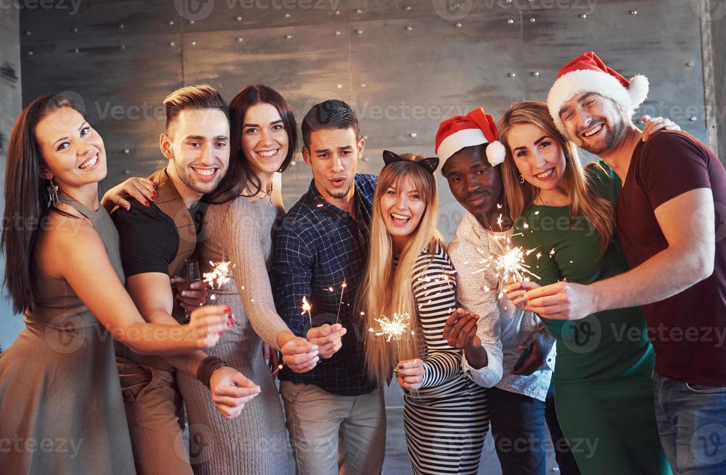Party mit Freunden. Gruppe fröhlicher junger Leute, die Wunderkerzen und Champagnerflöten tragen foto