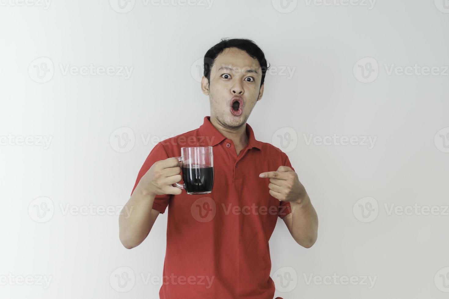 junger asiatischer mann, der eine tasse kaffee hält, die über lokalisiertem weißem hintergrund mit schock- und wow-ausdruck steht foto