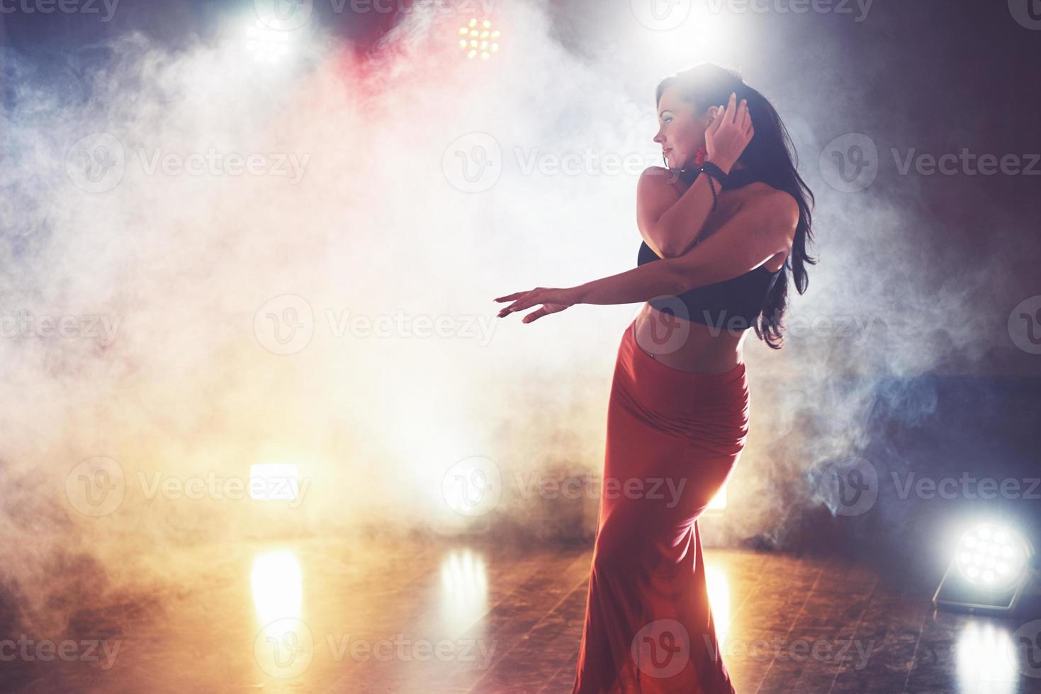 Geschicktes und schönes Tänzermädchen, das im dunklen Raum unter Konzertlicht und Rauch auftritt und einen künstlerischen und emotionalen zeitgenössischen Tanz aufführt foto