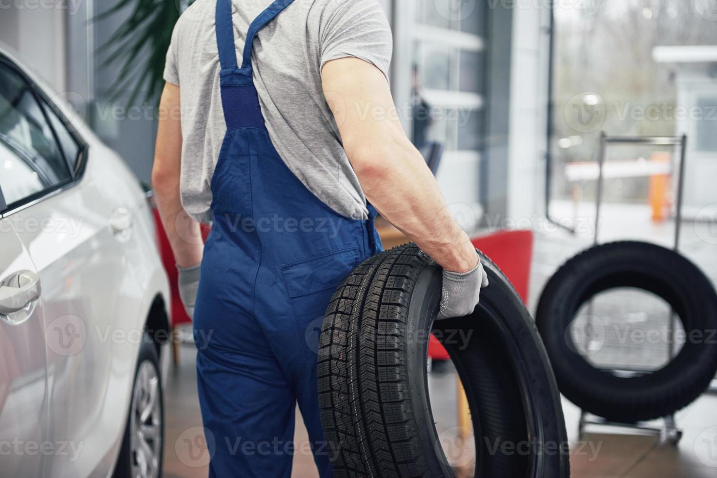 Mechaniker, der einen Reifen in der Werkstatt hält. Wechsel von Winter- und Sommerreifen foto