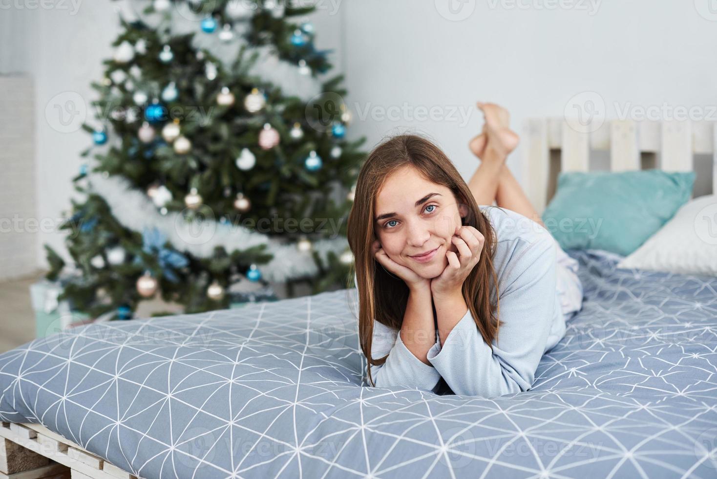 Schönes Mädchen liegt am Weihnachtsmorgen auf einem Bett im Schlafanzug foto