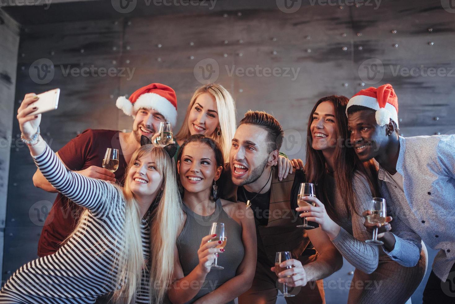 Gruppe schöne junge Leute, die Selfie in der Neujahrsparty machen, beste Freunde, Mädchen und Jungen, die zusammen Spaß haben und emotionale Lifestyle-Leute posieren. Hüte Weihnachtsmänner und Sektgläser in den Händen foto