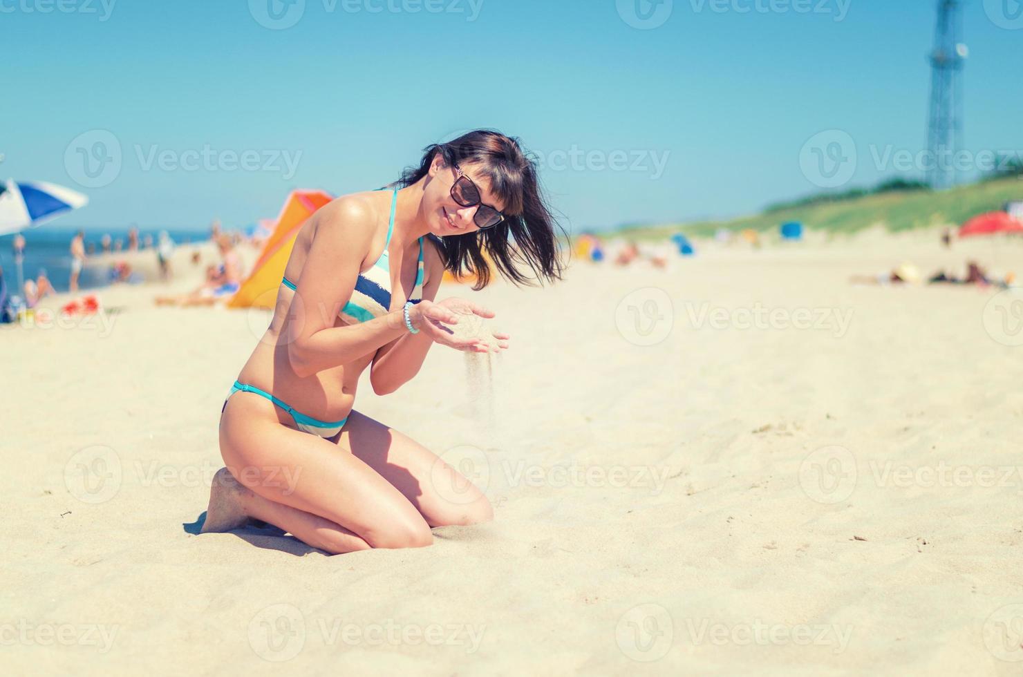 junge schöne Mädchen im Bikini sitzen am Sandstrand foto