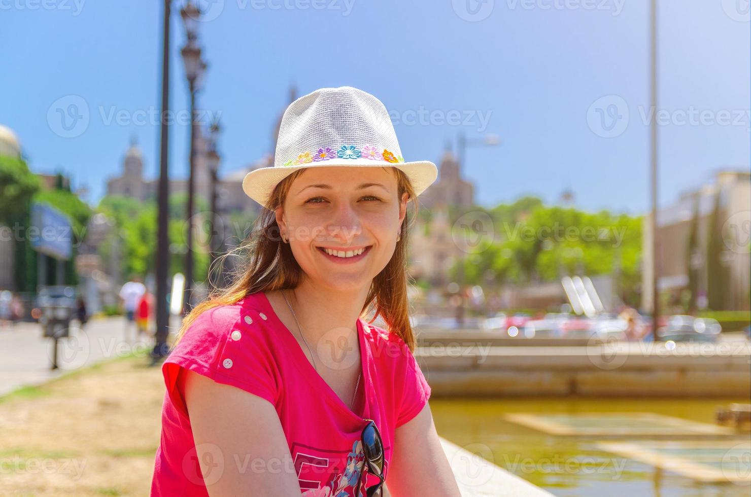 junge reisende mit rotem kleid und hut sitzt an einem sonnigen sommertag in der nähe des brunnens in barcelona foto