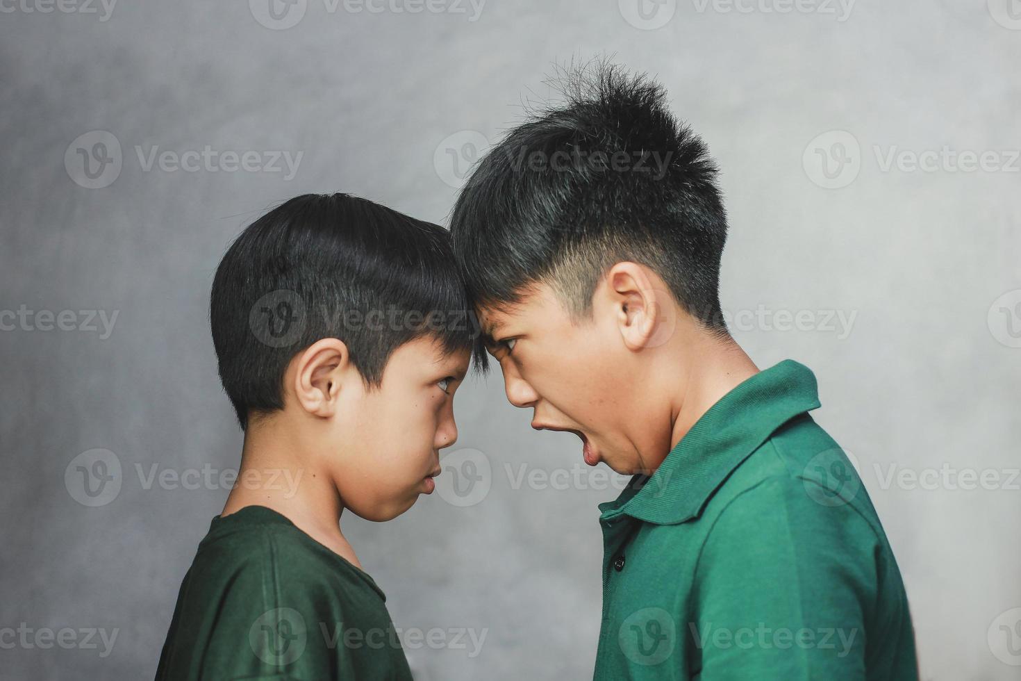 Zwei Geschwister schauen sich an und der große Bruder schreit vor seinem kleinen Bruder auf grauem Hintergrund foto
