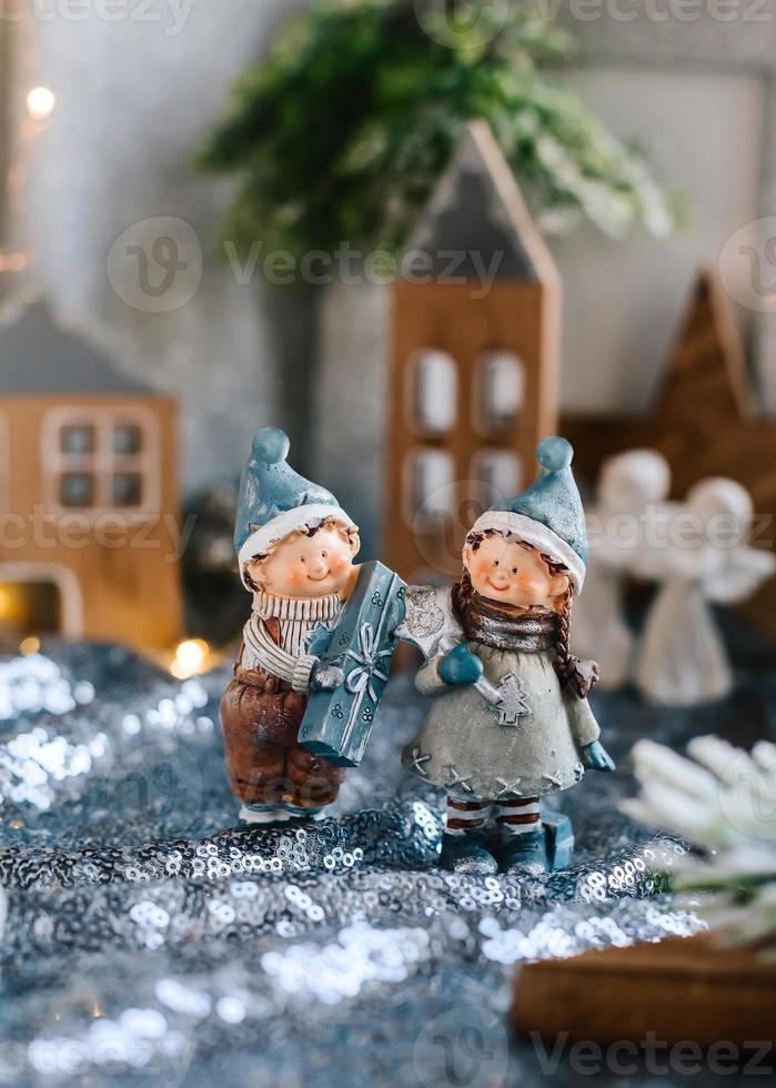 Porzellanfiguren von Kindern in einem Weihnachtsdekor. Winterfiguren eines Jungen und eines Mädchens mit Geschenken auf dem Hintergrund von Häusern und Kegeln. Weihnachtsgrußkarte. Platz kopieren. foto