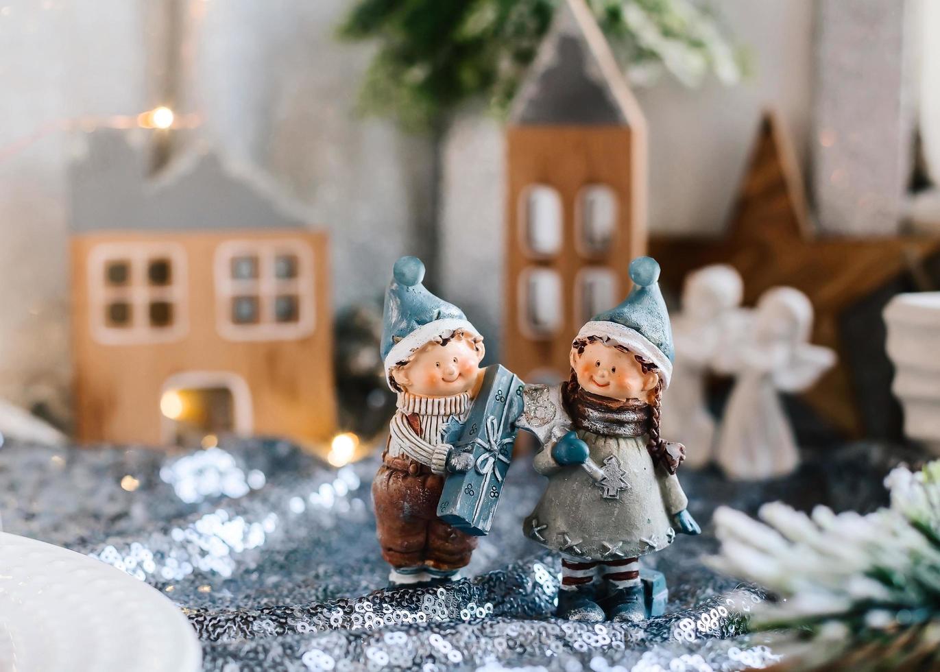 Porzellanfiguren von Kindern in einem Weihnachtsdekor. Winterfiguren eines Jungen und eines Mädchens mit Geschenken auf dem Hintergrund von Häusern und Kegeln. Weihnachtsgrußkarte. Platz kopieren. foto
