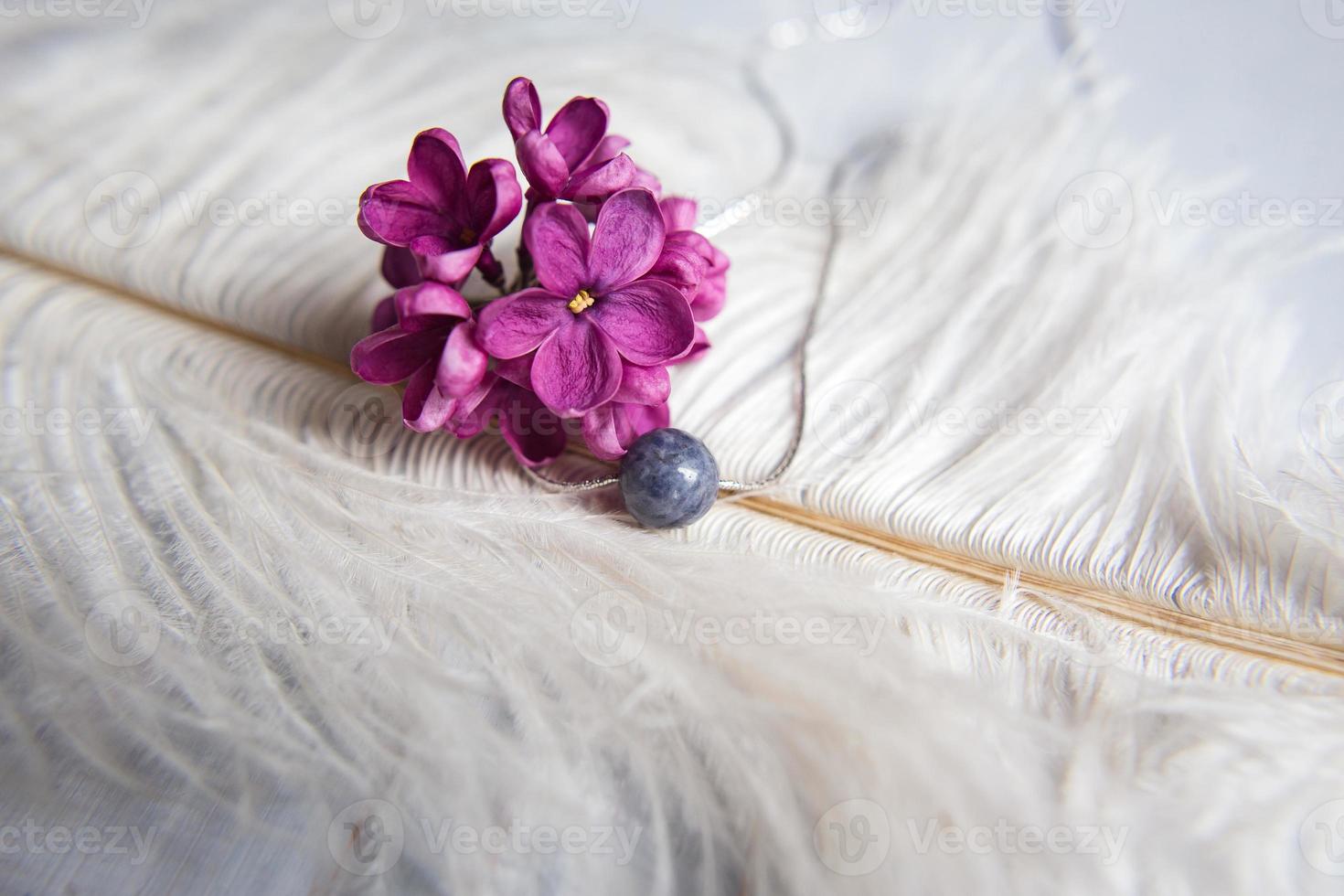 Halskette aus Naturstein mit silbernen Beschlägen mit lila-violett-lila Blüten auf weißer Straußenfeder. silberne Accessoires. foto