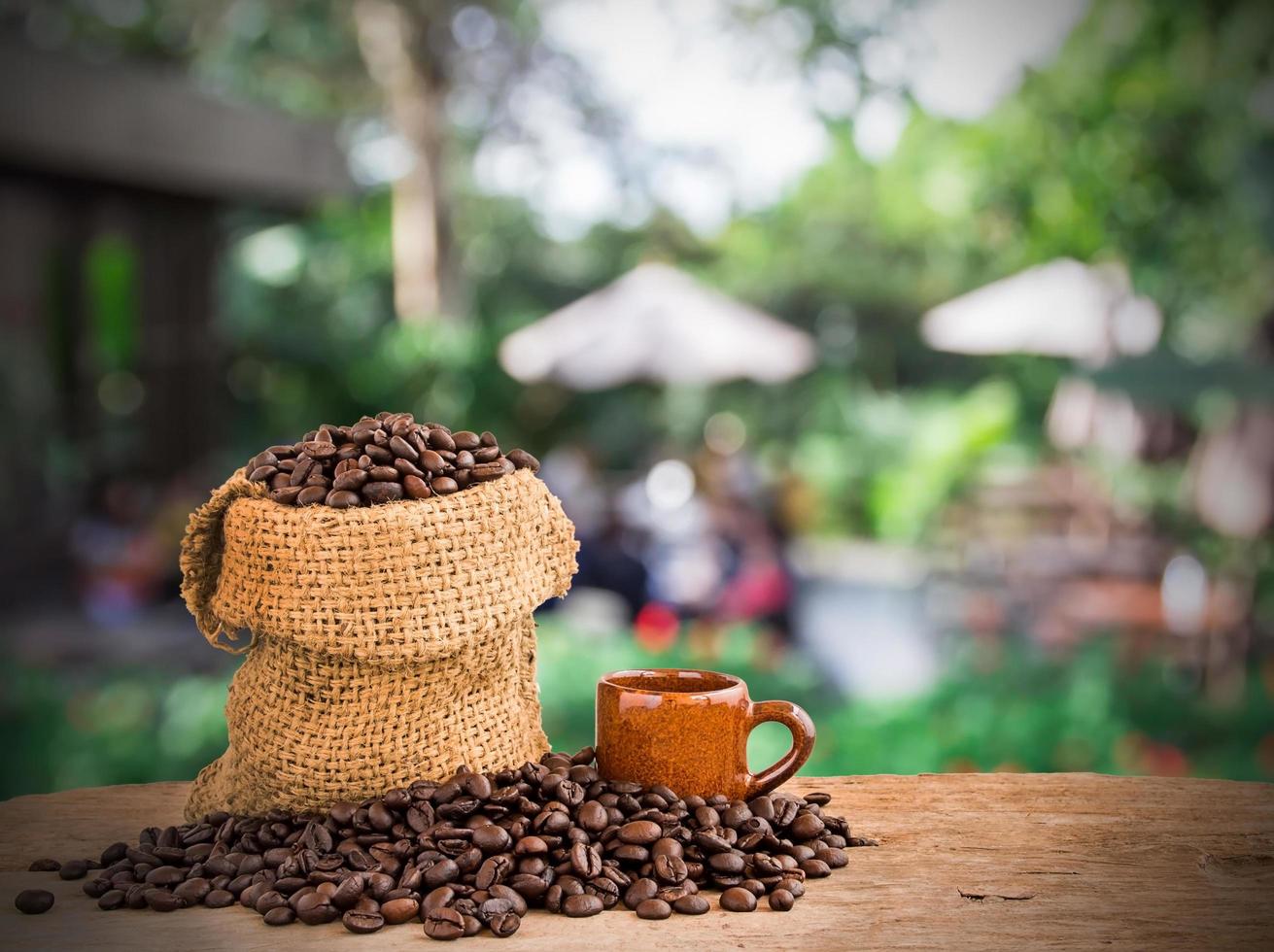 kaffeebohnen im leinensack auf holz des unscharfen caféhintergrundes foto