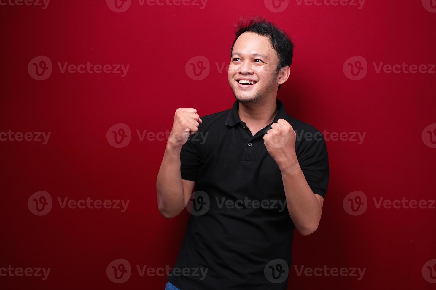 glücklicher aufgeregter und lächelnder junger asiatischer mann, der seinen arm hochhebt, um erfolg oder leistung zu feiern. foto