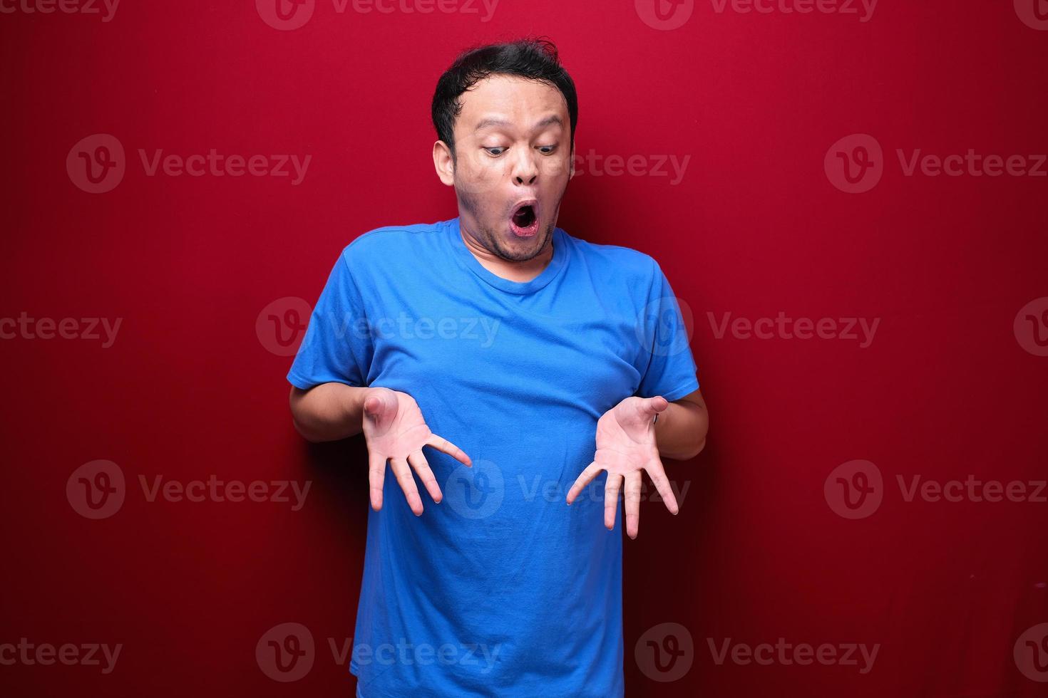 wow junger asiatischer mann ist überrascht und schreit mit nach unten zeigender hand auf rotem hintergrund. foto