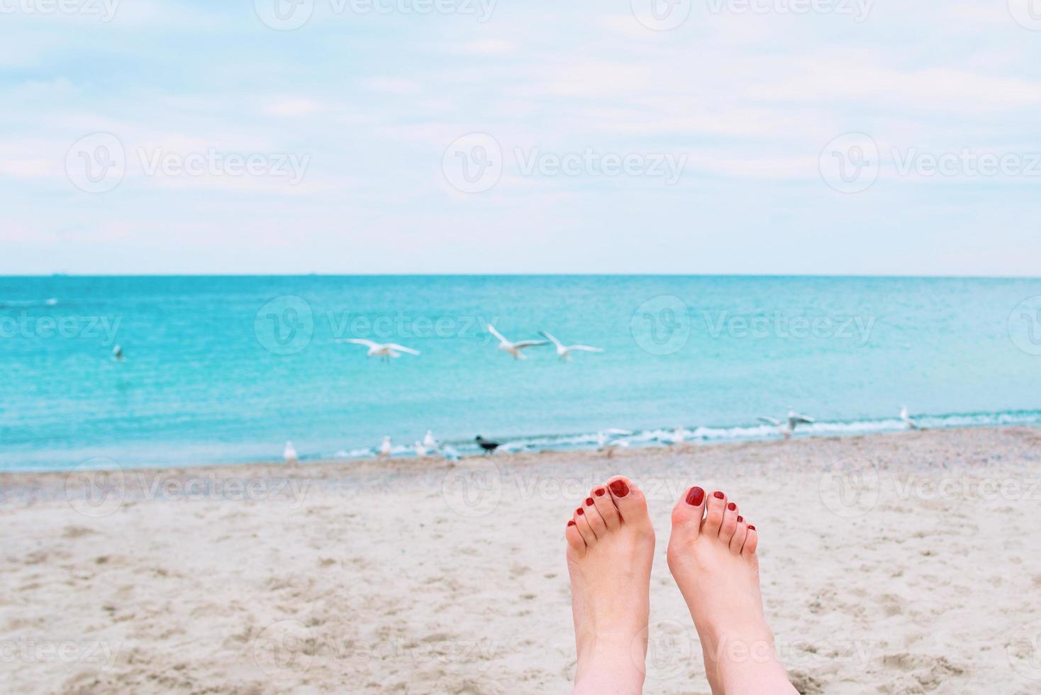 Frauenfüße mit roten Nägeln auf dem Hintergrund der Küste foto