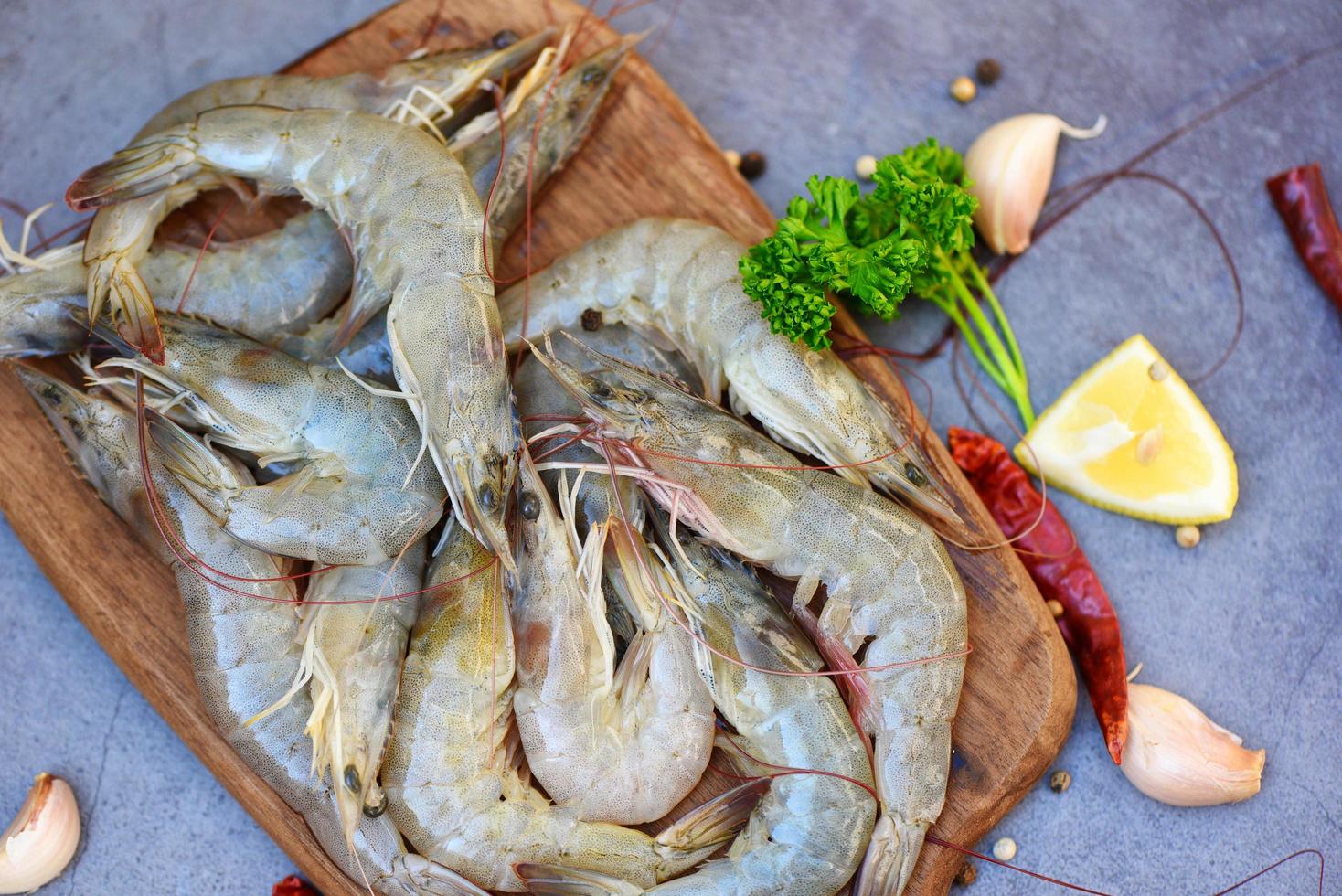 Rohe Garnelen auf dunklem Teller, frische Garnelengarnelen zum Kochen mit Gewürzen, Zitrone, Knoblauch, schwarzer Pfeffer, Chili auf Holzschneidebrett im Fischrestaurant foto