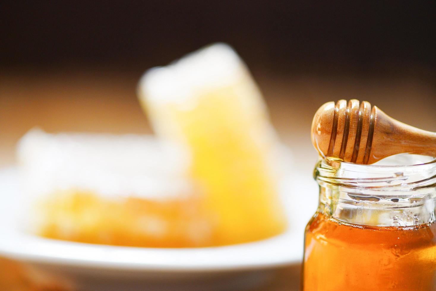 frischer honig süß im glasglas mit holzschöpflöffel - wabe, honigbienenhintergrund foto