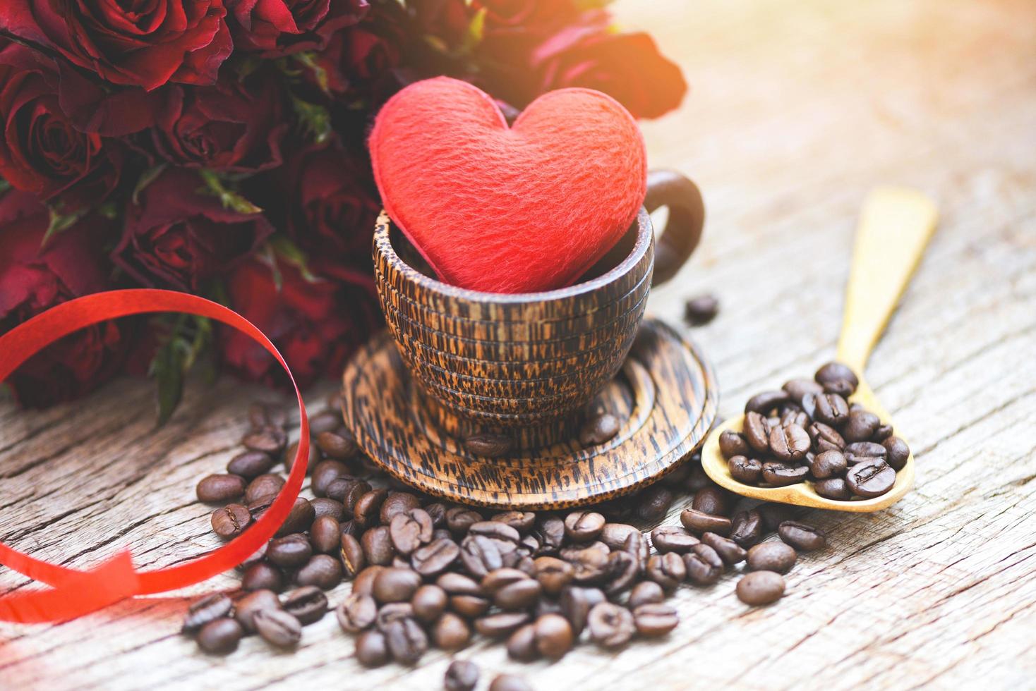 Herz in hölzerner Kaffeetasse mit Kaffeebohnen romantischer Liebes-Valentinstag und roter Rosenblume auf hölzernem Hintergrund - Liebeskaffeekonzept foto