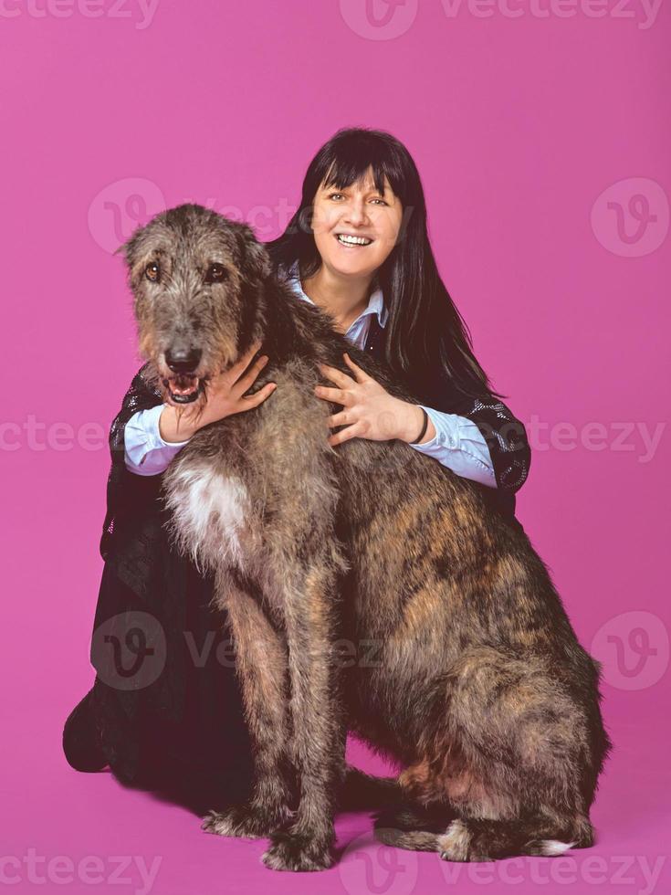 lächelnde, fröhliche, brünette Frau mit grauen irischen Wolfshunden auf fuchsiafarbenem Hintergrund im Fotostudio. freundschaft, liebe, haustierkonzept. foto