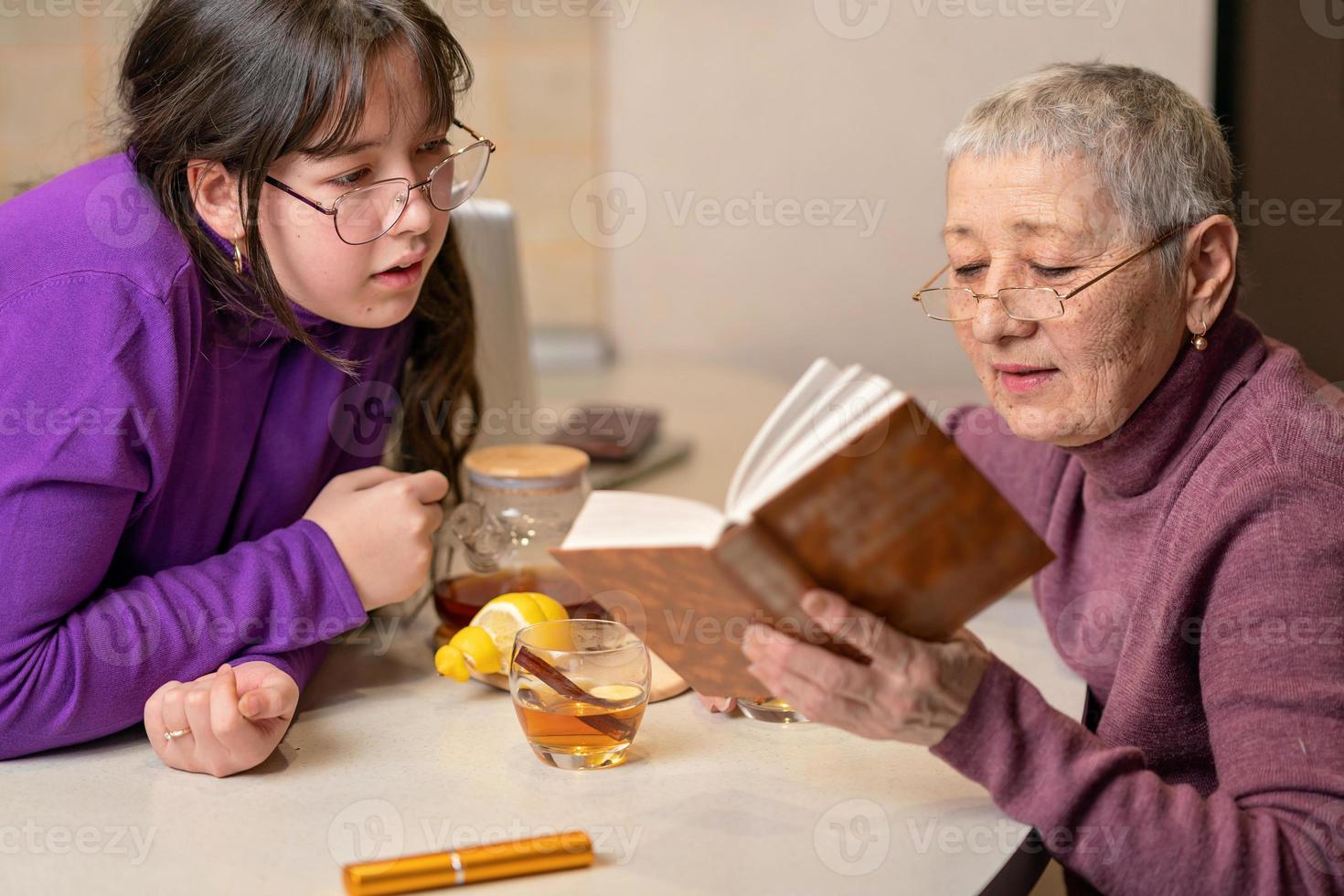 großmutter und enkelin trinken tee am tisch sitzend und lesen ein buch. foto