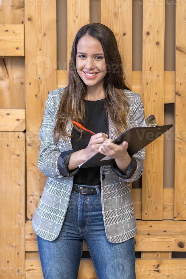 lächelnde Frau mit Stift und Tablet in der Nähe einer Holzwand foto