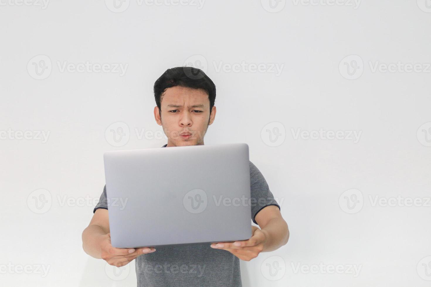 wow gesicht ihres asiatischen mannes schockiert, was er auf dem laptop auf isoliertem grauem hintergrund sieht. foto