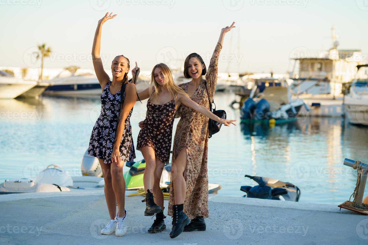 Fröhliche, vielfältige Freunde, die auf einem Pier in der Nähe des Meeres stehen foto