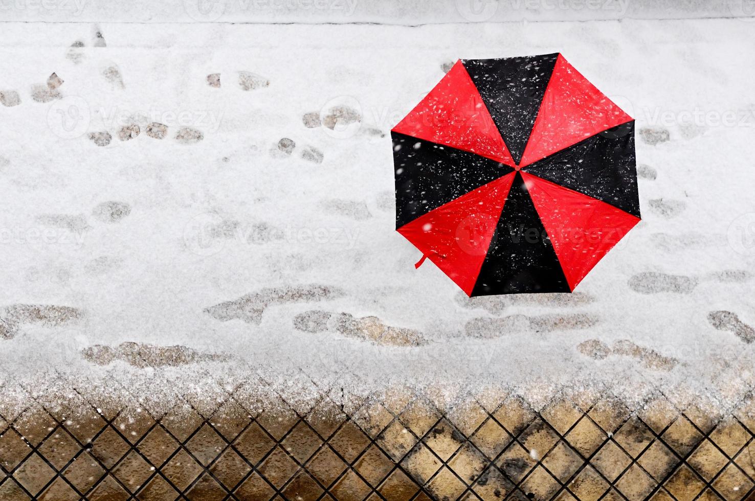 Frau, die einen schwarzen und roten Regenschirm unter Schnee hält foto