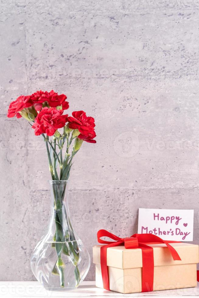 Kann Muttertag handgefertigte Geschenkbox wünscht Fotografie - schöne blühende Nelken mit roter Schleifenbox isoliert auf fair-faced grauem Hintergrund Schreibtisch, Nahaufnahme, Kopierraum, Mock-up foto
