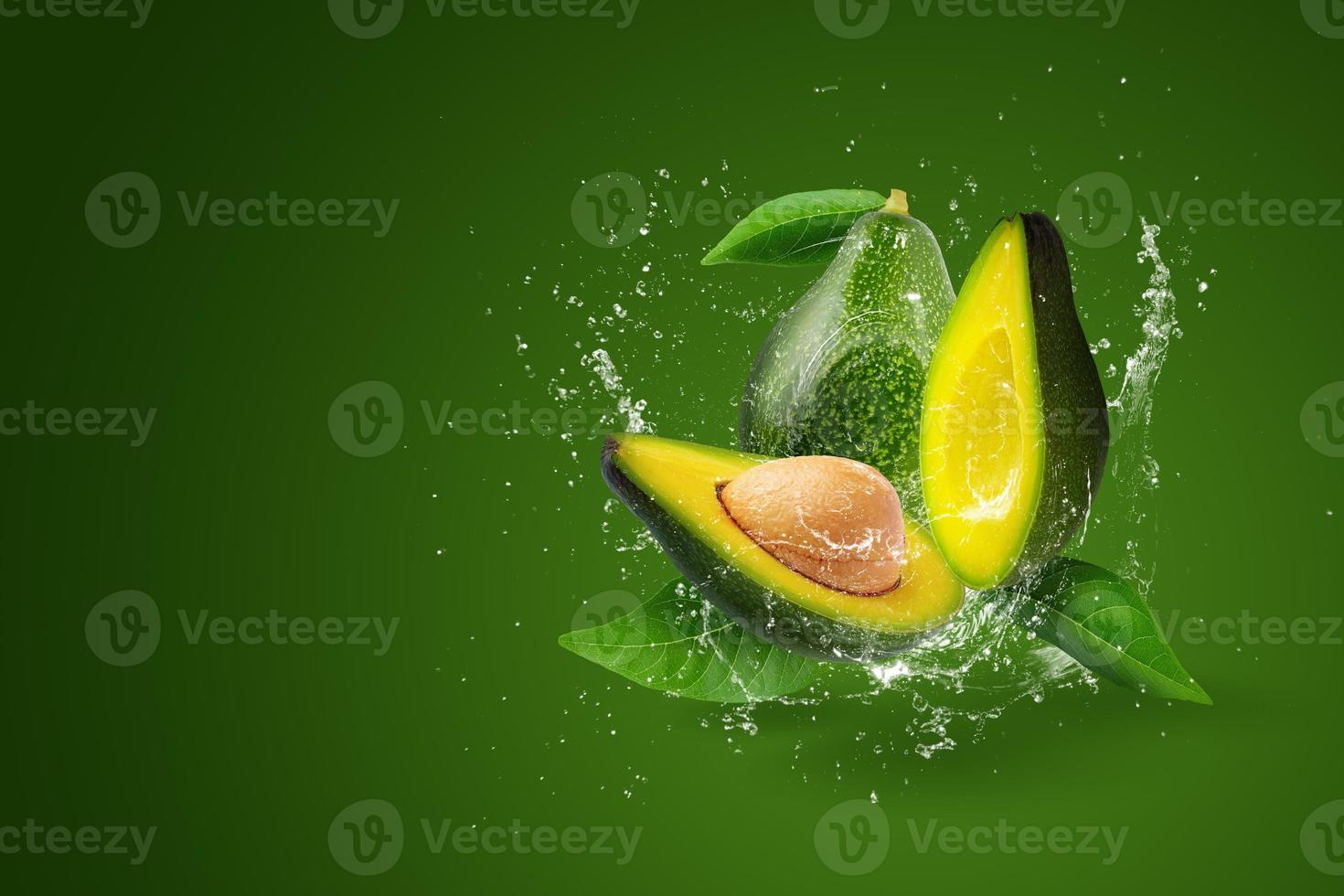 Wasser spritzt auf grüne reife Avocado auf grünem Hintergrund. foto