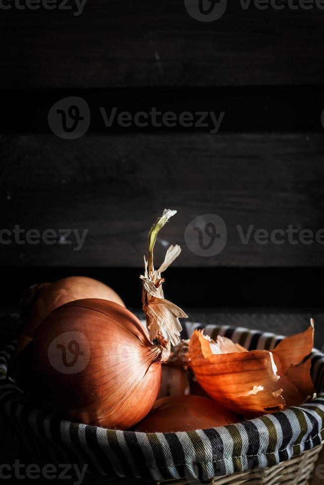 Zwiebeln in einem Weidenkorb mit Holzbrettern im Hintergrund. rustikaler Stil. vertikales Bild. foto