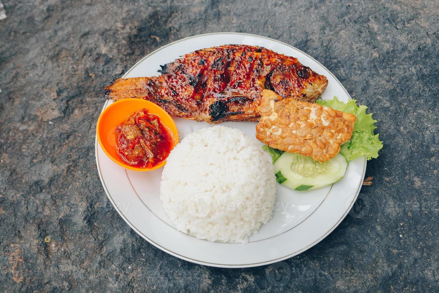 Köstlicher gegrillter Tilapia aus Indonesien mit Reis, Tempeh, Gemüse und Chilisauce im Teller foto