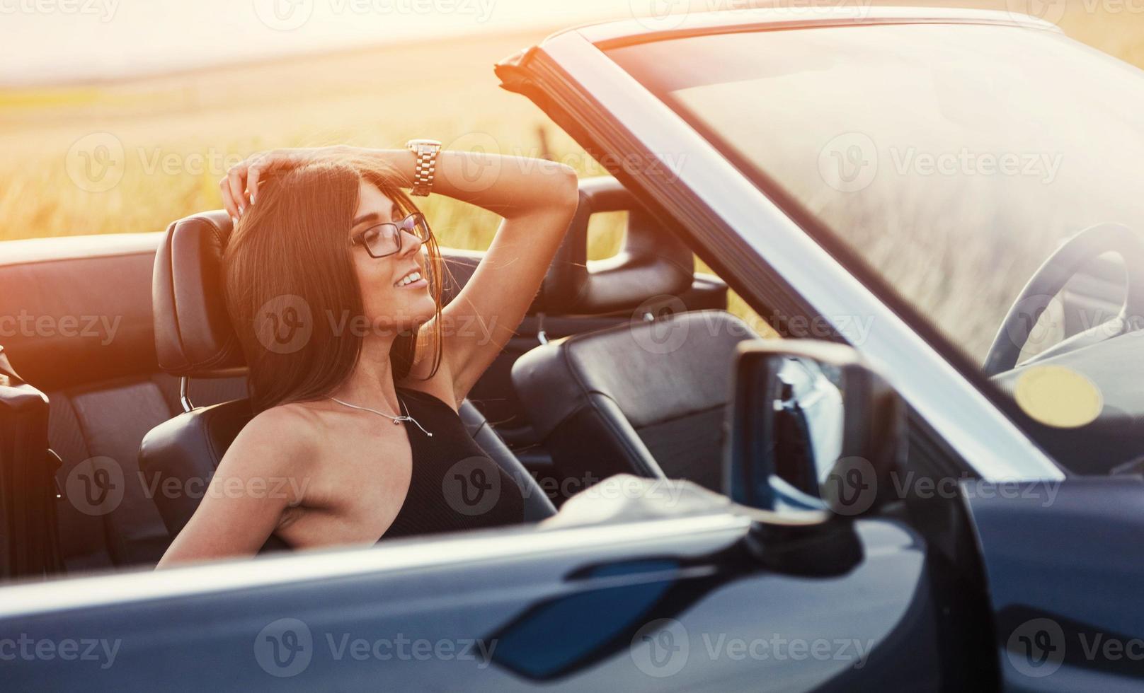 schöne junge frau, die nahe einem auto auf der straße aufwirft foto