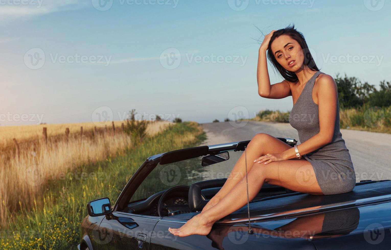 schöne junge frau, die nahe einem auto auf der straße aufwirft foto