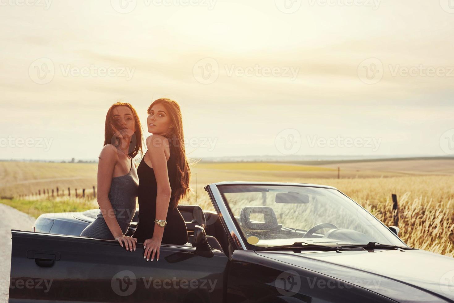 zwei sexy brünette frau, die in der nähe ihres autos steht foto