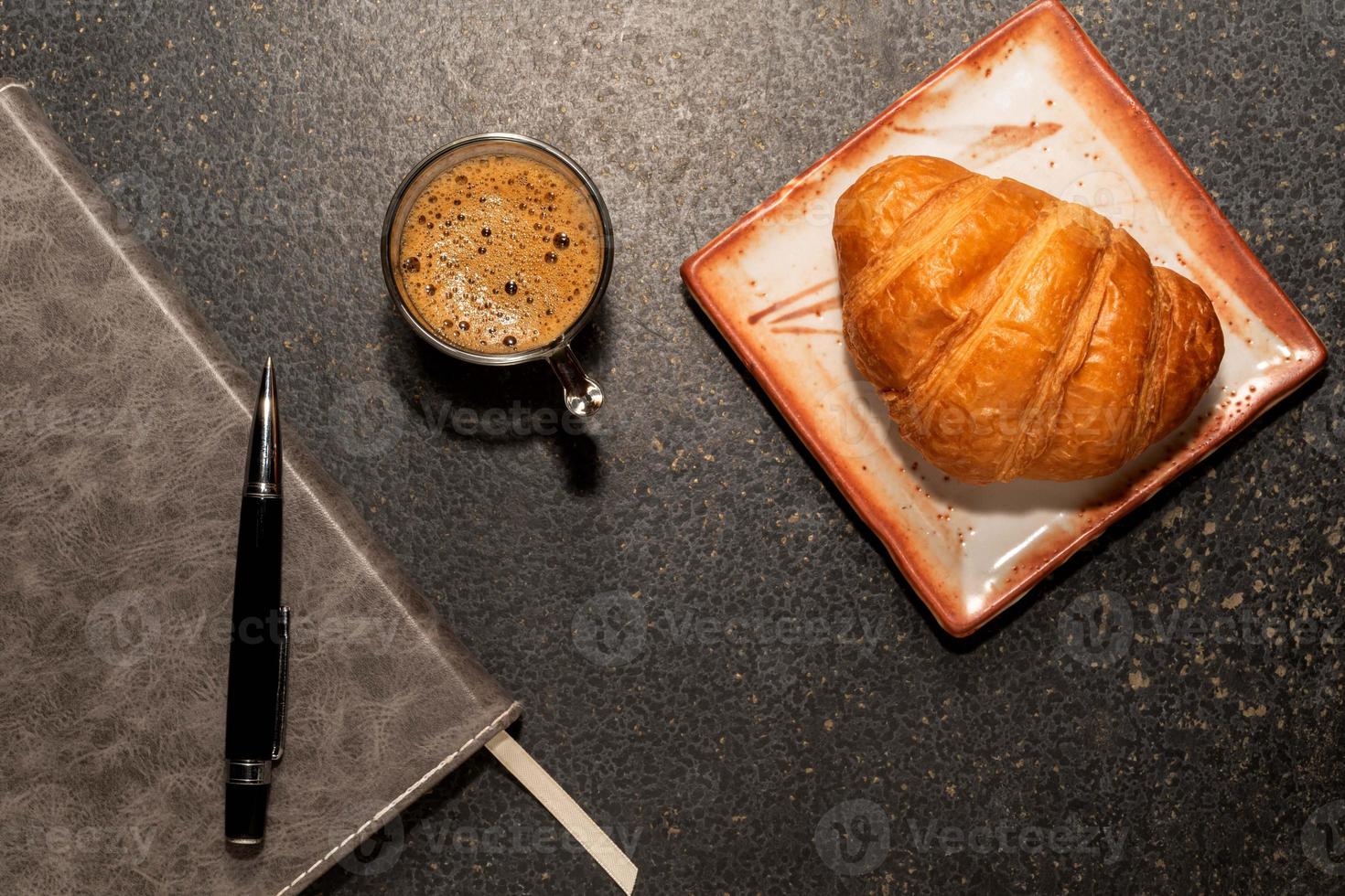 frühstückscroissant in teller und kaffee auf steintisch. foto