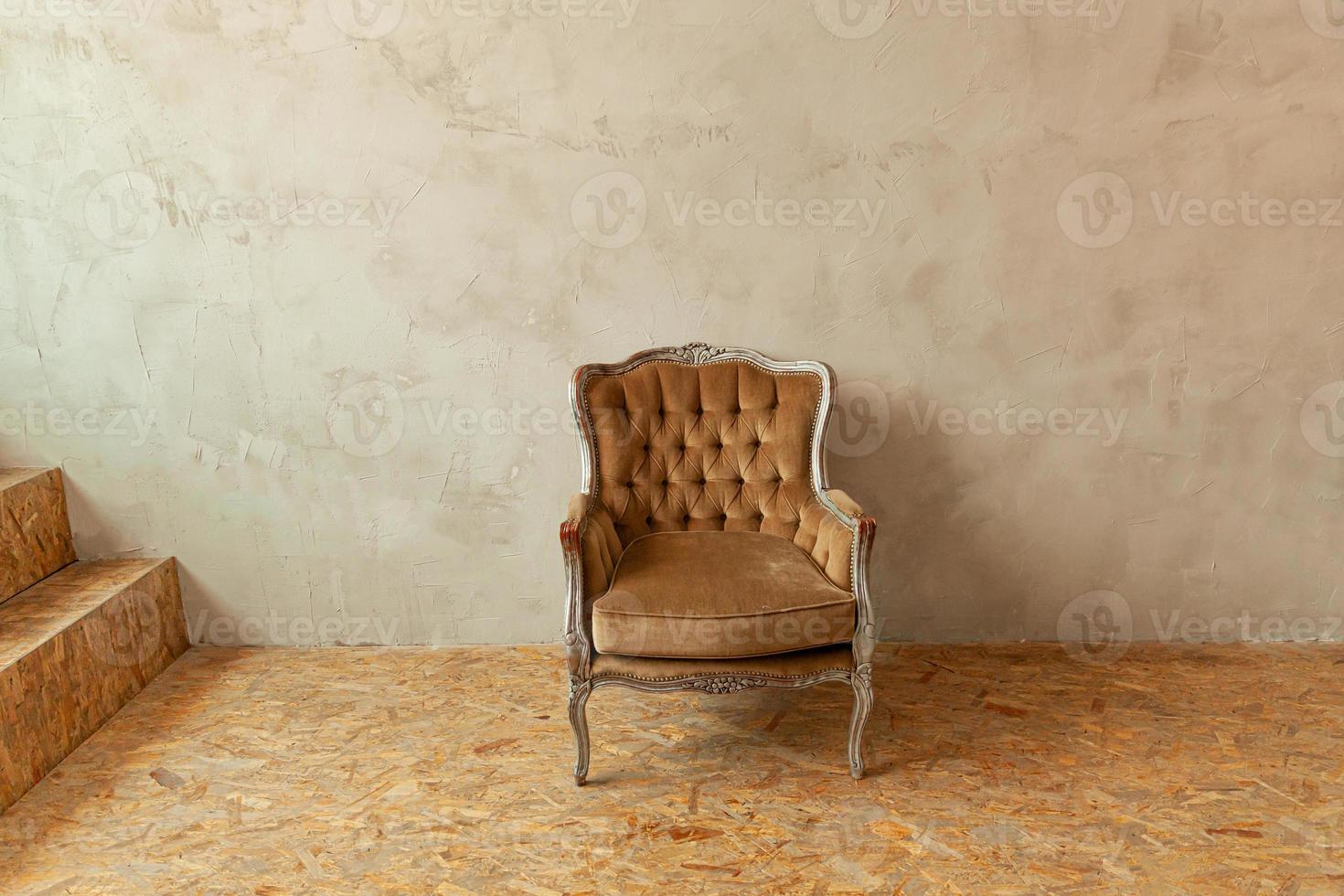 schöner luxus klassischer biege sauberer innenraum im grunge-stil mit braunem barocksessel. vintage antiker braungrauer stuhl neben der wand. minimalistisches Wohndesign. foto