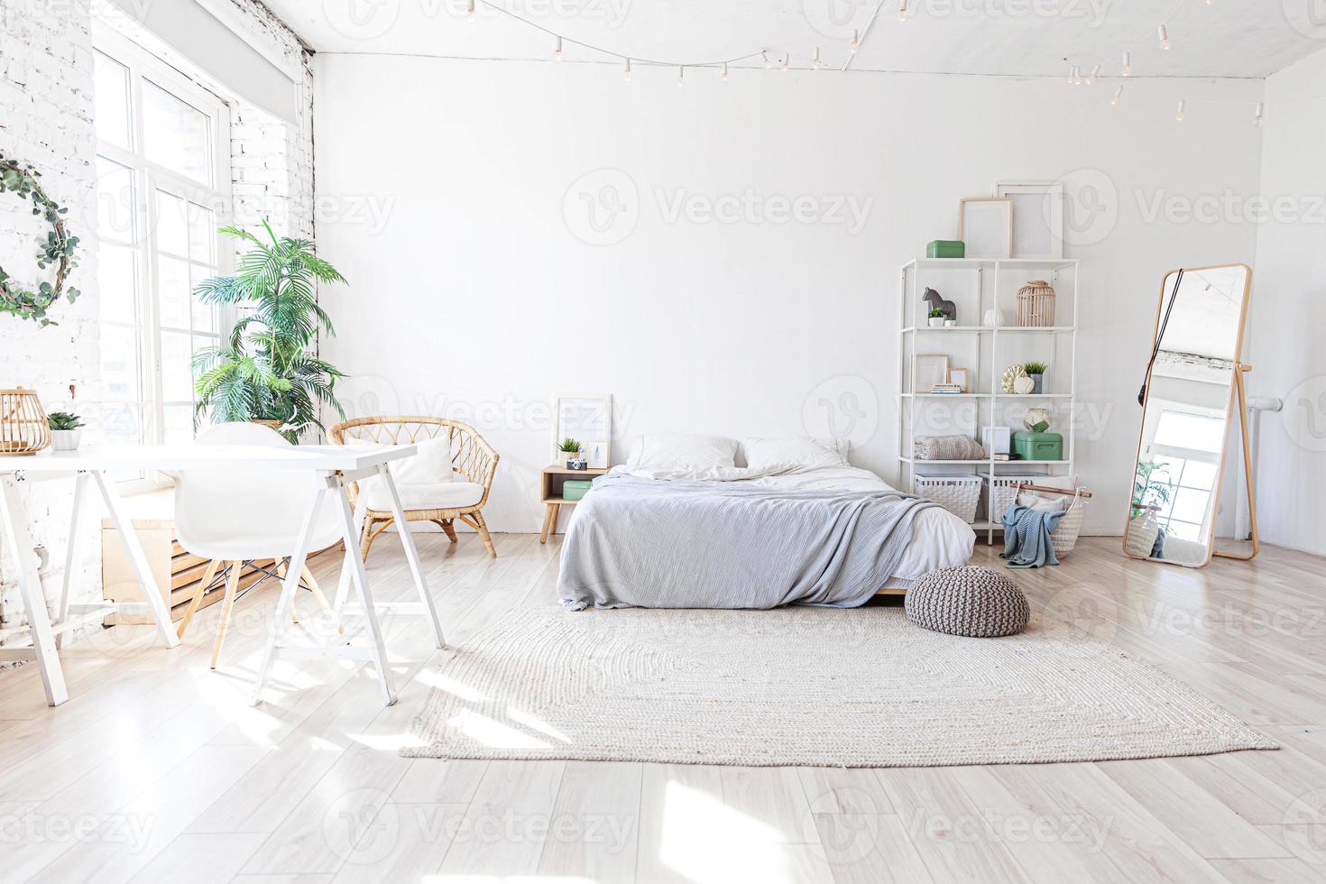 stilvolles Loft-Schlafzimmer-Interieur. Geräumiges Design-Apartment mit hellen Wänden, großen Fenstern, großem Bett. saubere moderne dekoration mit eleganten möbeln im minimalistischen skandinavischen stil. foto