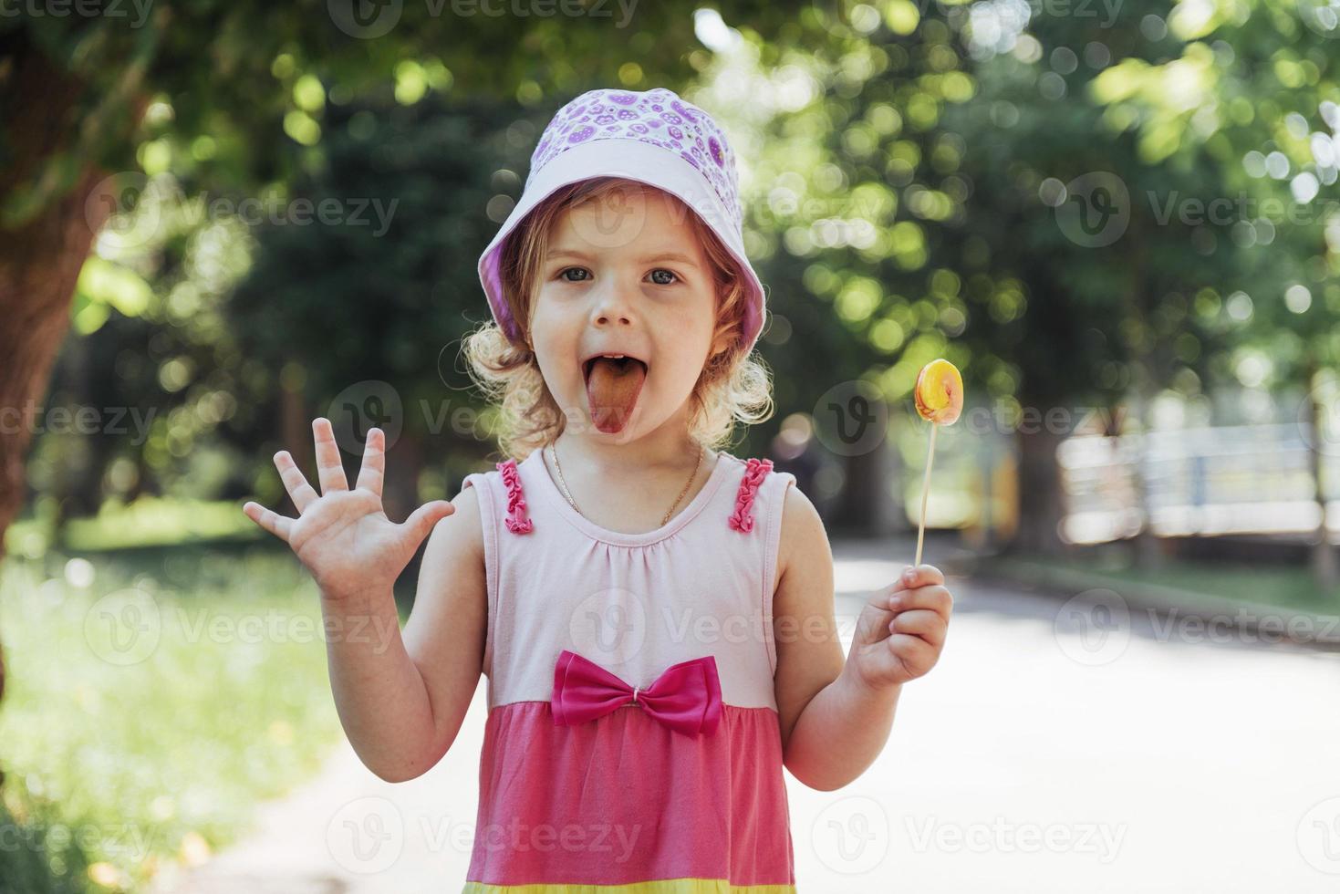 lustiges kind mit bonbonlutscher, glückliches kleines mädchen, das groß isst foto