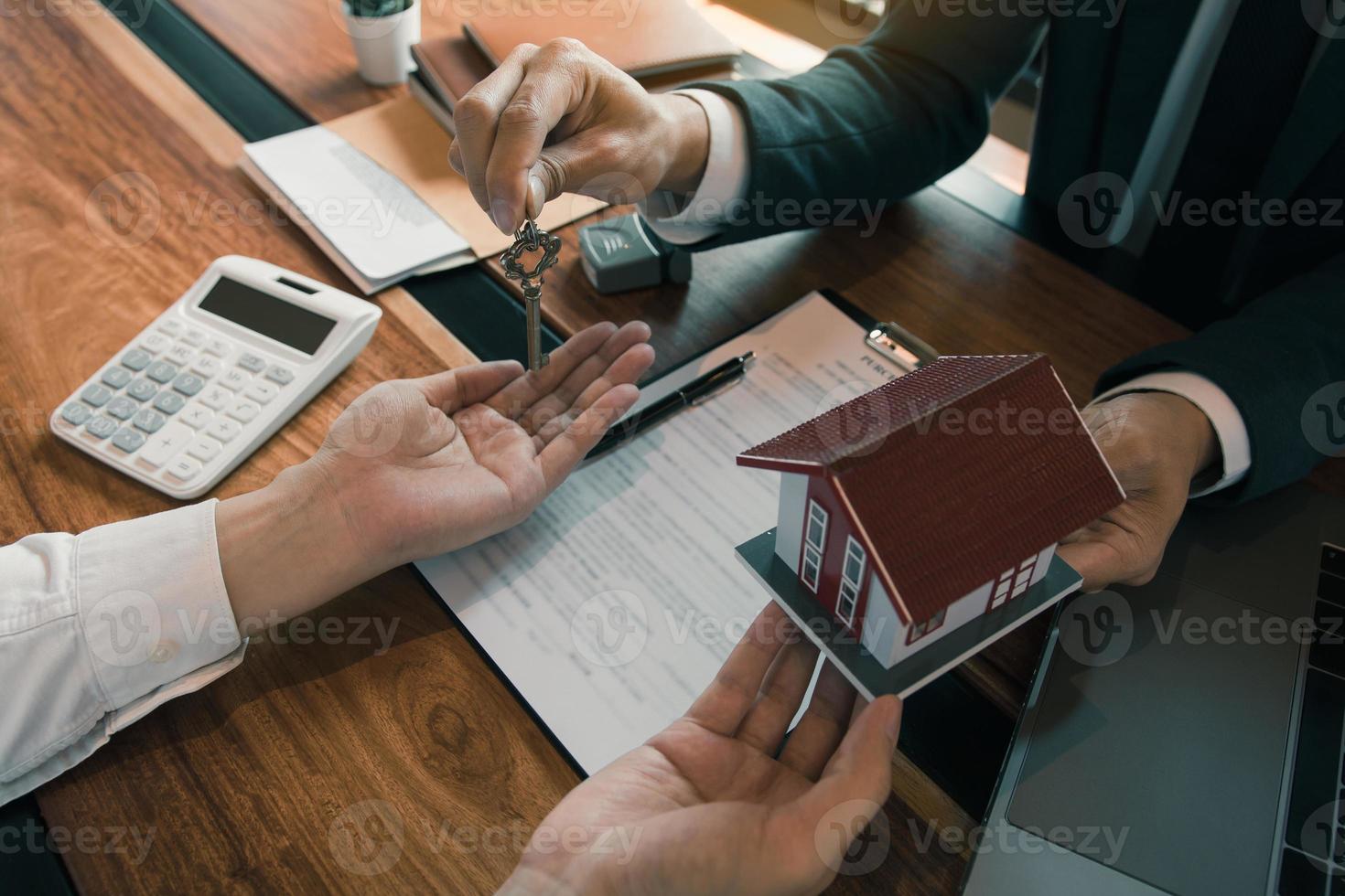 die hand des immobilienmaklers übergibt den schlüssel an neue hausbesitzer im büro mit käuferhauskonzept. foto