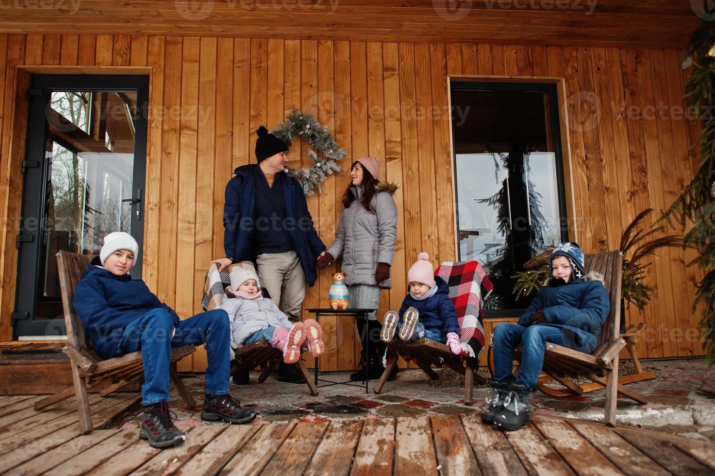 große junge Familie mit vier Kindern auf der Terrasse eines Holzhauses am Wintertag. foto