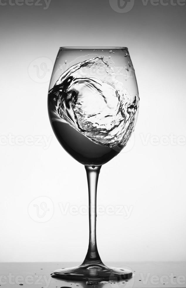 ein Spritzer Wasser in ein Glas Weinglas. Spritzwasser im Glas auf leuchtendem Hintergrund. transparente Flüssigkeit, die in Weinglas spritzt. Essen, Objekt. foto